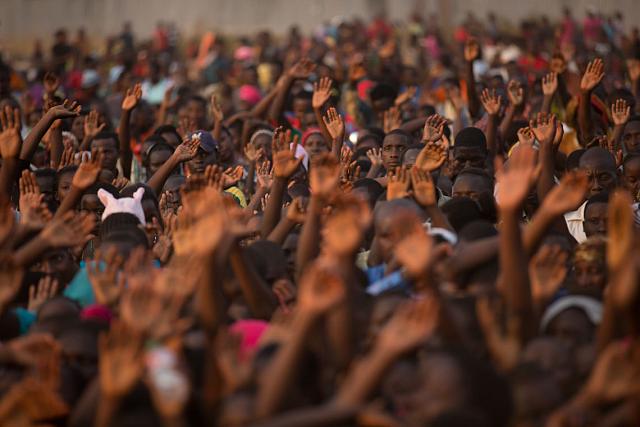 Une foule de personnes, quelque part en Afrique, lèvent les mains au ciel. 